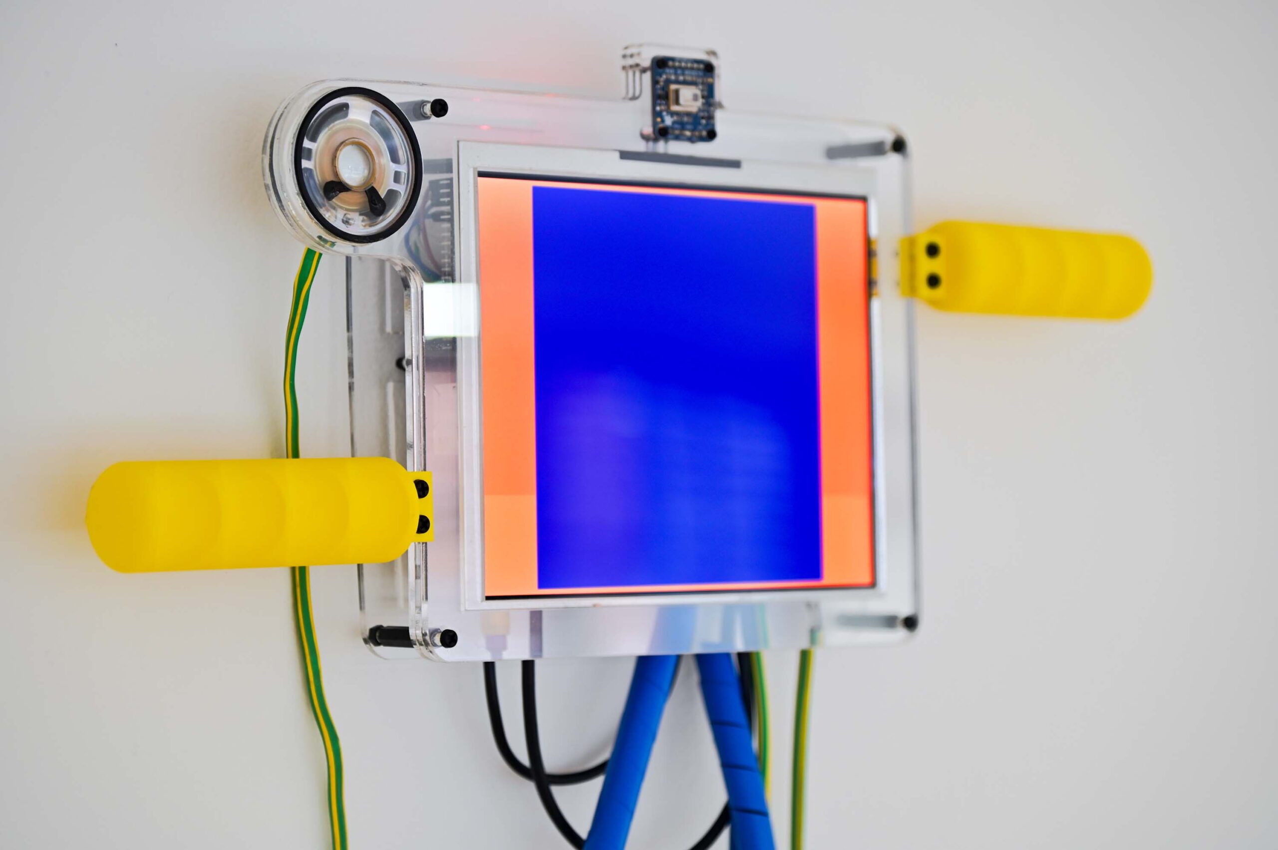 close-up of artwork with brightly coloured cables, 3d printed parts and a large screen.